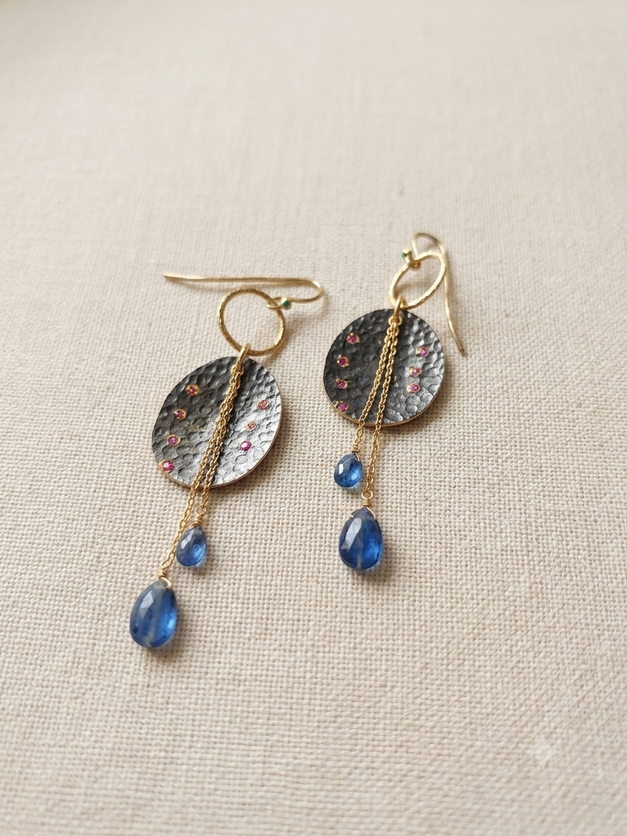 A pair of handmade dangle earrings featuring textured hammered silver discs with tiny pink ruby accents, gold-toned chains, and iolite drops.Sterling silver.