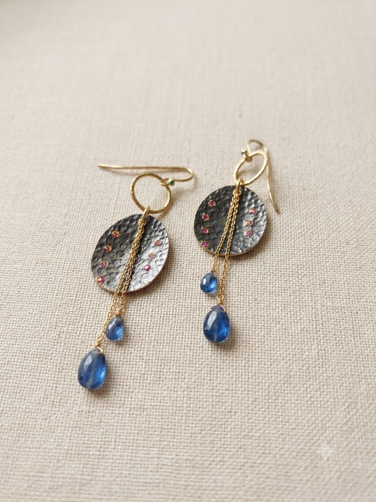 A pair of handmade dangle earrings featuring textured hammered silver discs with tiny pink ruby accents, gold-toned chains, and iolite drops.Sterling silver.
